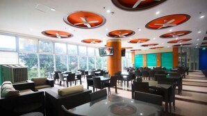 A spacious indoor area with multiple tables and chairs, ceiling fans, and large windows providing natural light. - UPad Hotel (Manila)