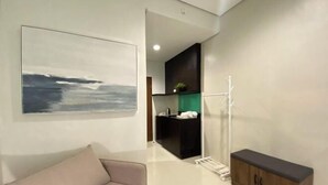 A modern hotel room with a large abstract painting, a minimalist kitchenette, a built-in cabinet, and a glass shower enclosure. - UPad Hotel (Manila)