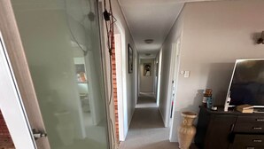 A hallway with a sliding glass door, a dark-colored cabinet with a flat-screen TV, and a tiled floor. - That 70s House - 5 bedroom of comfort and history (Ayr)