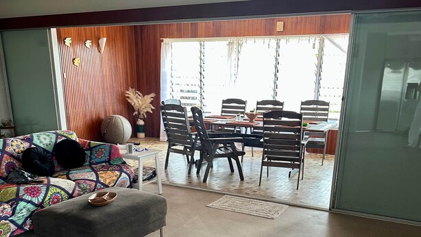 A spacious living area with a sofa, ottoman, and a dining table with chairs. There is a sliding glass door leading to an outdoor patio area. - That 70s House - 5 bedroom of comfort and history (Ayr)