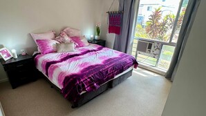 A bedroom with a bed, a ceiling fan, a nightstand, a bedside table, a window with a view of greenery, and a balcony. - That 70s House - 5 bedroom of comfort and history (Ayr)