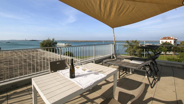 Een balkon met uitzicht op zee, een tafel met fles en glas, en een stoel.