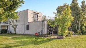 Een modern gebouw met een plat dak, een balkon en een kleine tuin met bomen en gras.