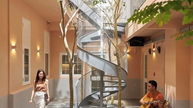 A modern indoor space with a spiral staircase, a person playing guitar, and another walking. - Express by M Village Nam Ky Khoi Nghia, a brand of Modern Village Lifestyle (Ho Chi Minh City)