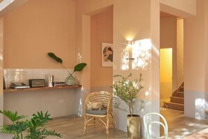 A room with a wooden floor, a chair, a potted plant, a wall-mounted light fixture, and a staircase in the background. - Express by M Village Nam Ky Khoi Nghia, a brand of Modern Village Lifestyle (Ho Chi Minh City)