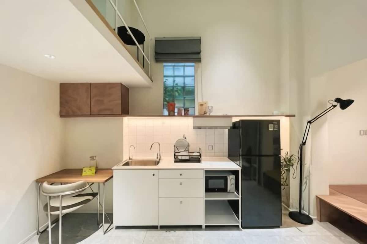 Une cuisine moderne avec des meubles blancs, un réfrigérateur noir, une table à manger avec des chaises et un petit comptoir.