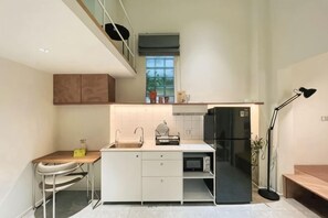 Eine moderne Küche mit weißen Schränken, einem schwarzen Kühlschrank, einem Esstisch mit Stühlen und einer kleinen Arbeitsfläche.