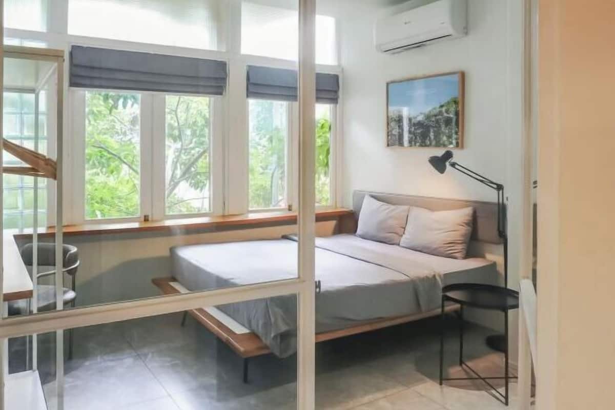 Une chambre à coucher comprenant un lit, un bureau, une chaise, une lampe et une fenêtre donnant sur un paysage verdoyant.