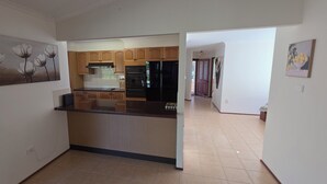 A kitchen with wooden cabinets, a black countertop, and a painting of flowers on the wall. - Skippers By The Bay - Lemon Tree Passage (Lemon Tree Passage)