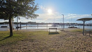 A sandy beach with a bench and picnic table, a dock with boats, and a clear sky. - Skippers By The Bay - Lemon Tree Passage (Lemon Tree Passage)