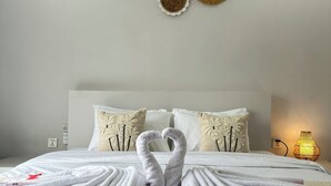 Un lit bien fait, avec des serviettes disposées en forme de cygne, une tête de lit blanche et des œuvres d’art décoratives accrochées au mur.