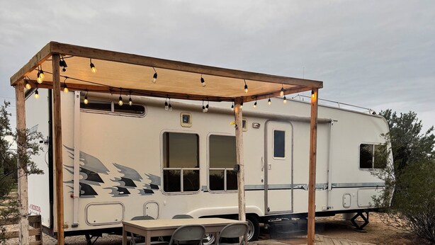 Ein Wohnmobil mit einer überdachten Terrasse, einer Feuerstelle und einem Tisch mit Stühlen.