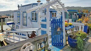 Une maison située sur la côte, aux couleurs bleu et blanc, avec une terrasse en bois et une grande plante en pot.