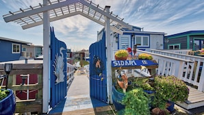 Une terrasse en bois avec une balustrade blanche, un portail bleu et une enseigne sur laquelle on peut lire « SIDARL ».