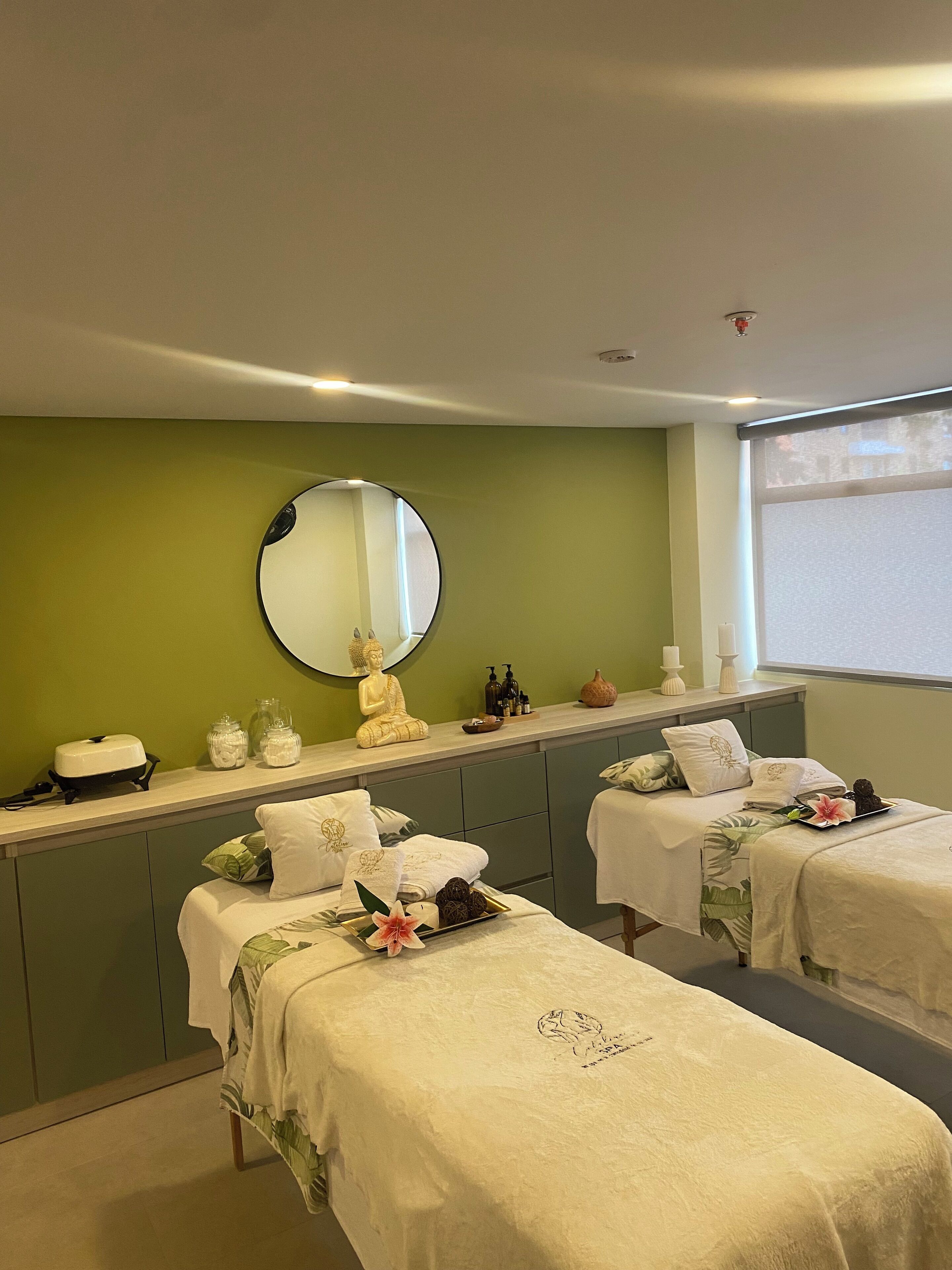 A spa room with two massage tables, a mirror, and a Buddha statue.
