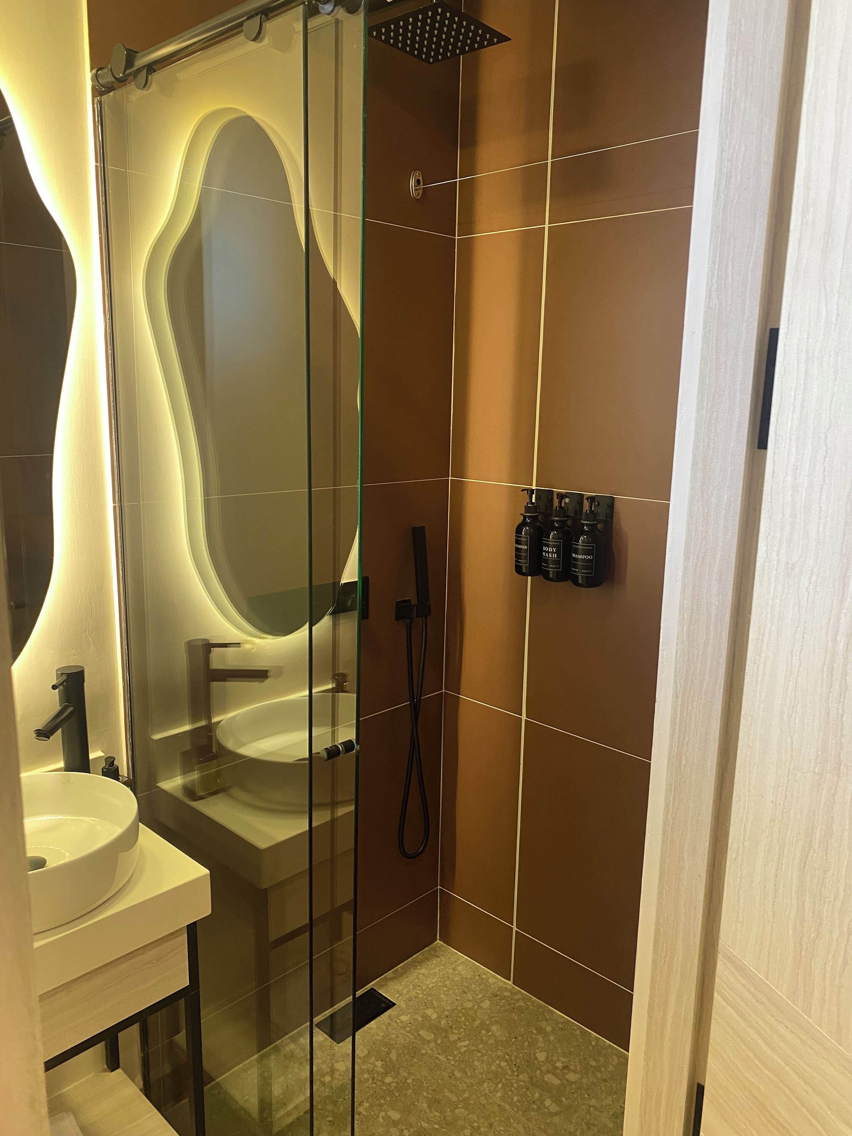 Een moderne badkamer met een douchecabine van glas, een witte wastafel en een douchekop aan de muur.