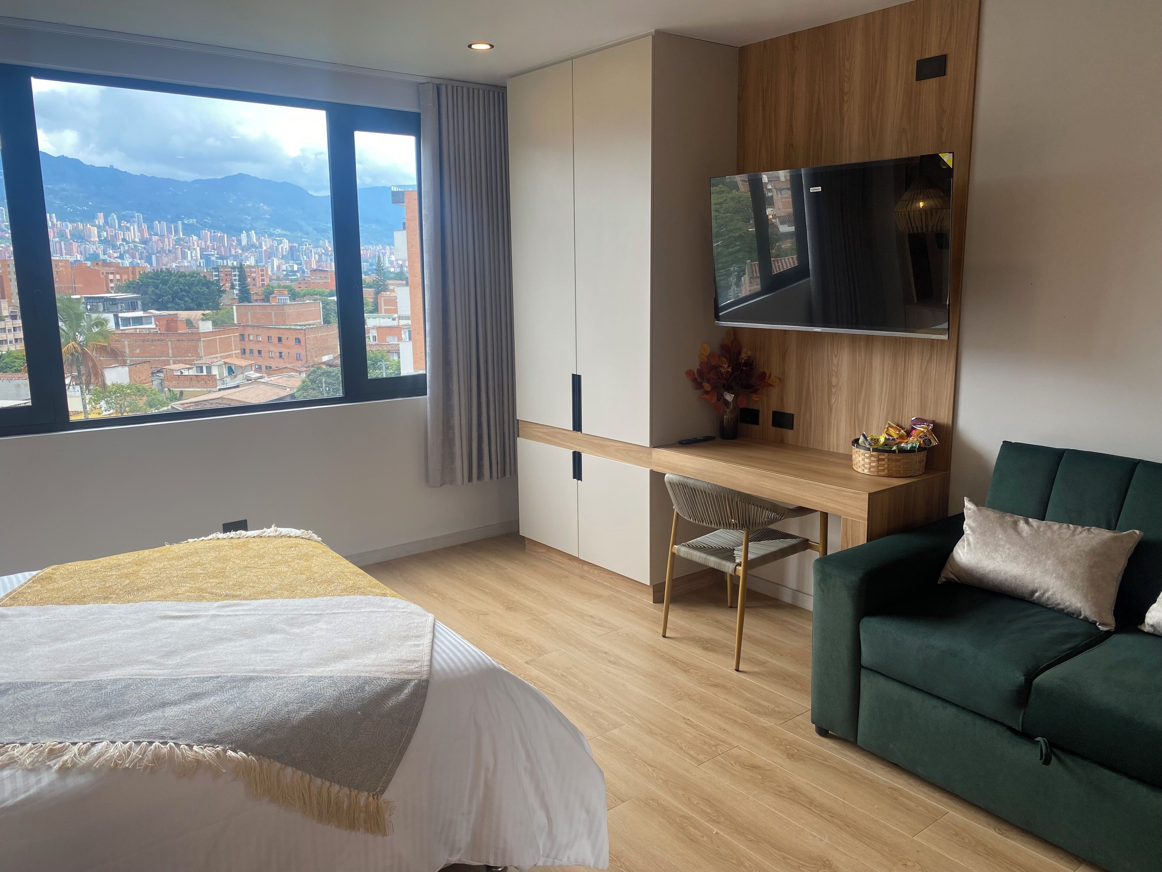 A modern hotel room with a large window, a desk, a green sofa, and a bed.