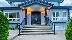 Une maison moderne à deux étages, dotée d’une façade en pierre, d’une porte d’entrée noire et d’un escalier menant à l’entrée.