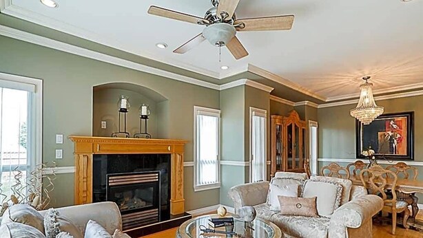 Un salon spacieux doté d’une cheminée, d’un ventilateur de plafond et d’un lustre.