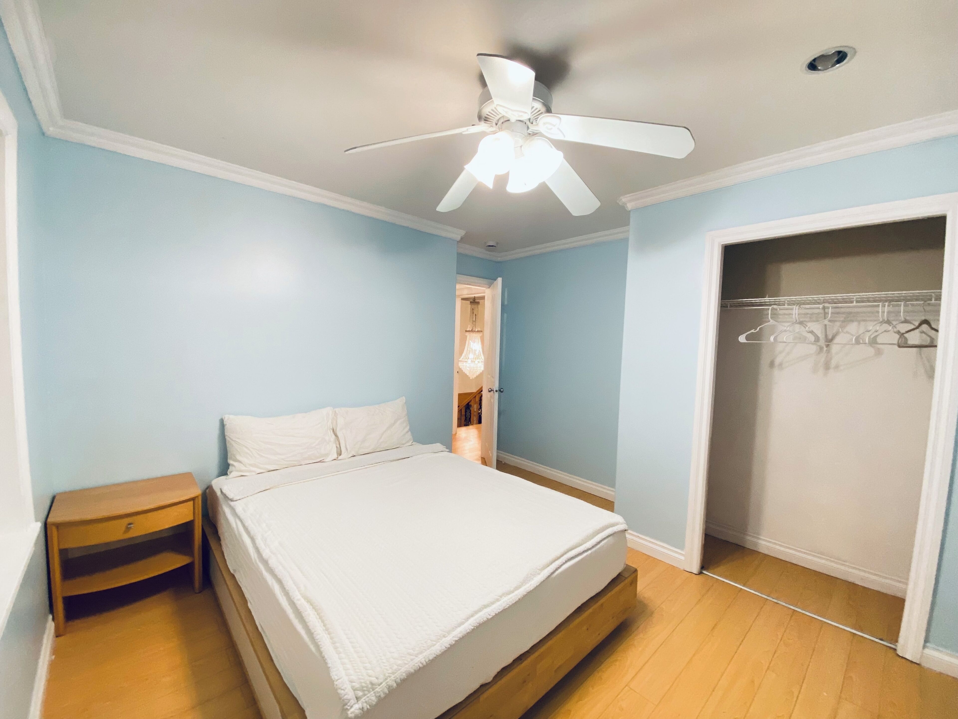 A bedroom with a bed, a nightstand, a ceiling fan, and a walk-in closet.