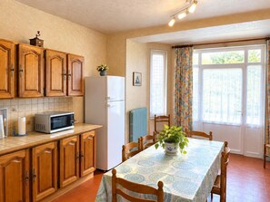 Una cocina con armarios de madera, un refrigerador, un microondas y una mesa de comedor con sillas.