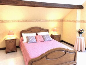 A bedroom with a wooden bed, two bedside tables with lamps, a decorative wall border, and a small table with a vase of flowers. - CHEZ MATHIEU - CHESTRES (CHESTRES)