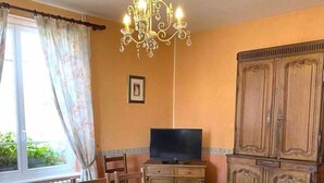 Una habitación con una mesa de comedor de madera, sillas, un televisor, un armario y una araña.
