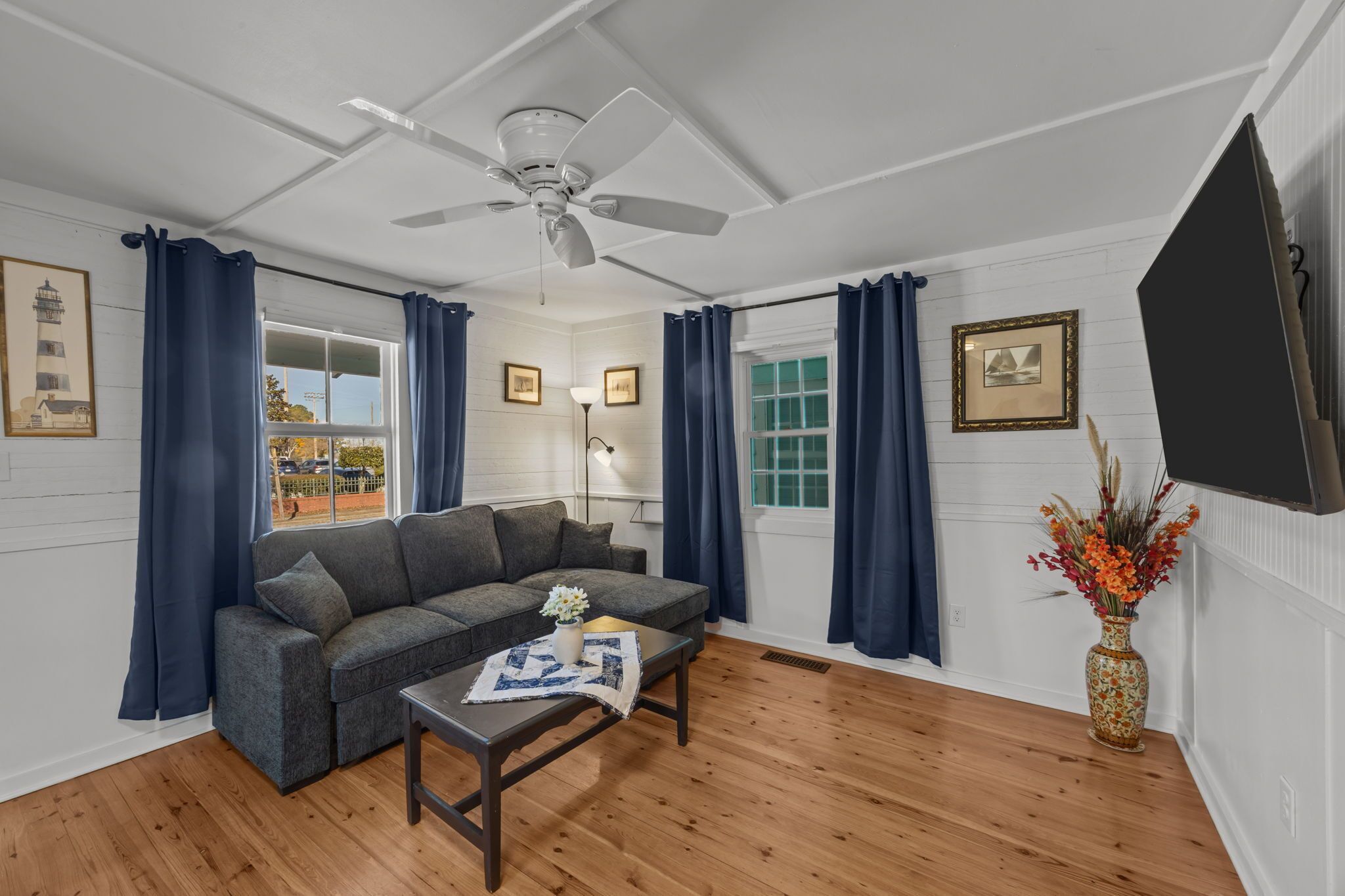 A living room with a gray sofa, a wooden coffee table, a ceiling fan, and a vase with flowers.