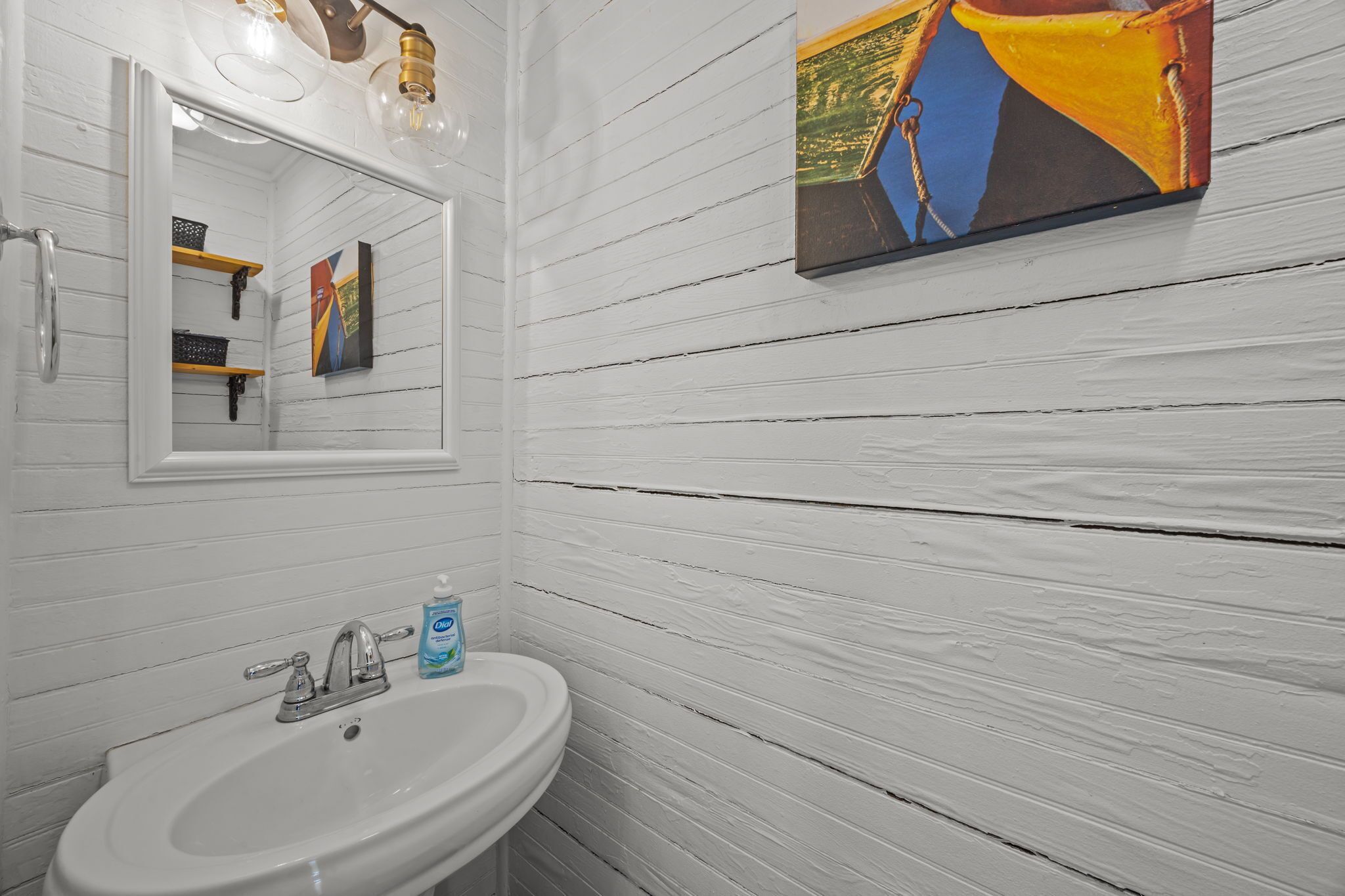 A bathroom with a white sink, a mirror, and a painting on the wall.