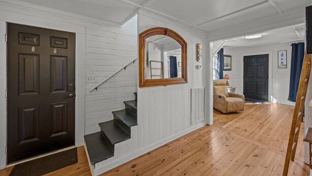 A staircase with a dark door, white paneled walls, and a wooden floor. - Historic Downtown New Bern Retreat - Pet Friendly (New Bern)