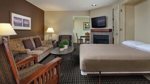 Quarto de hotel com uma cama, um sofá, uma mesinha de centro com abajur, televisão e lareira.