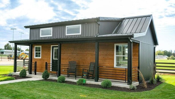 Ein zweistöckiges Gebäude mit Holzfassade und Metalldach, mit einer Veranda mit Stühlen und einem kleinen Garten.