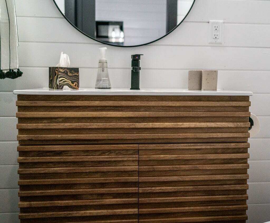 A bathroom vanity with a wooden finish, a mirror above it, and a white countertop.