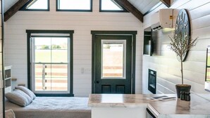 Una cocina compacta con una isla central, una zona de comedor con un banco y una pequeña zona de descanso con cama.
