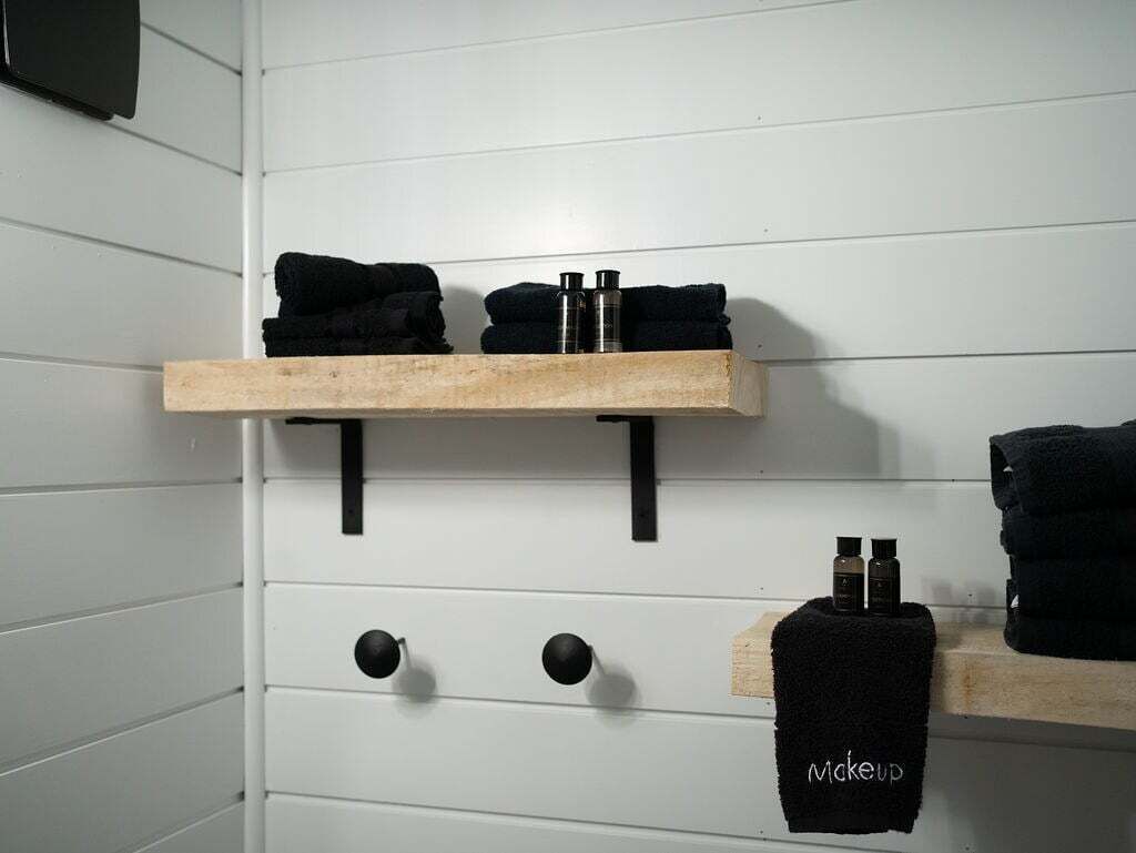 Une salle de bain avec un lambris blanc, deux porte-serviettes avec des serviettes noires et une étagère contenant des articles de toilette.