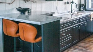 A modern kitchen with a central island, bar stools, a microwave, a coffee machine, and a clock on the wall.