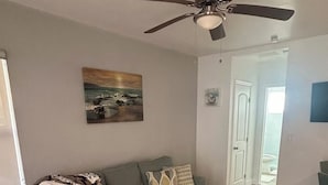 Un soggiorno con un divano grigio, una ventola a soffitto, un quadro e un pavimento in legno.