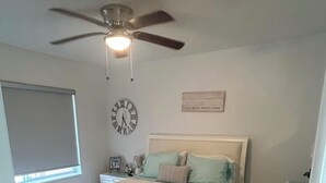 Una camera da letto con un letto, una ventola a soffitto, una sveglia, un comodino e una cassettiera.