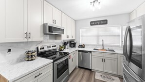 A modern kitchen with white cabinets, stainless steel appliances, and a marble countertop. - Game Room Retreat • Fire Pit • 5 Min to Downtown (Mount Dora)