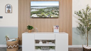 A reception area with a TV mounted on a wooden wall, a white reception desk, and a potted plant. - Game Room Retreat • Fire Pit • 5 Min to Downtown (Mount Dora)