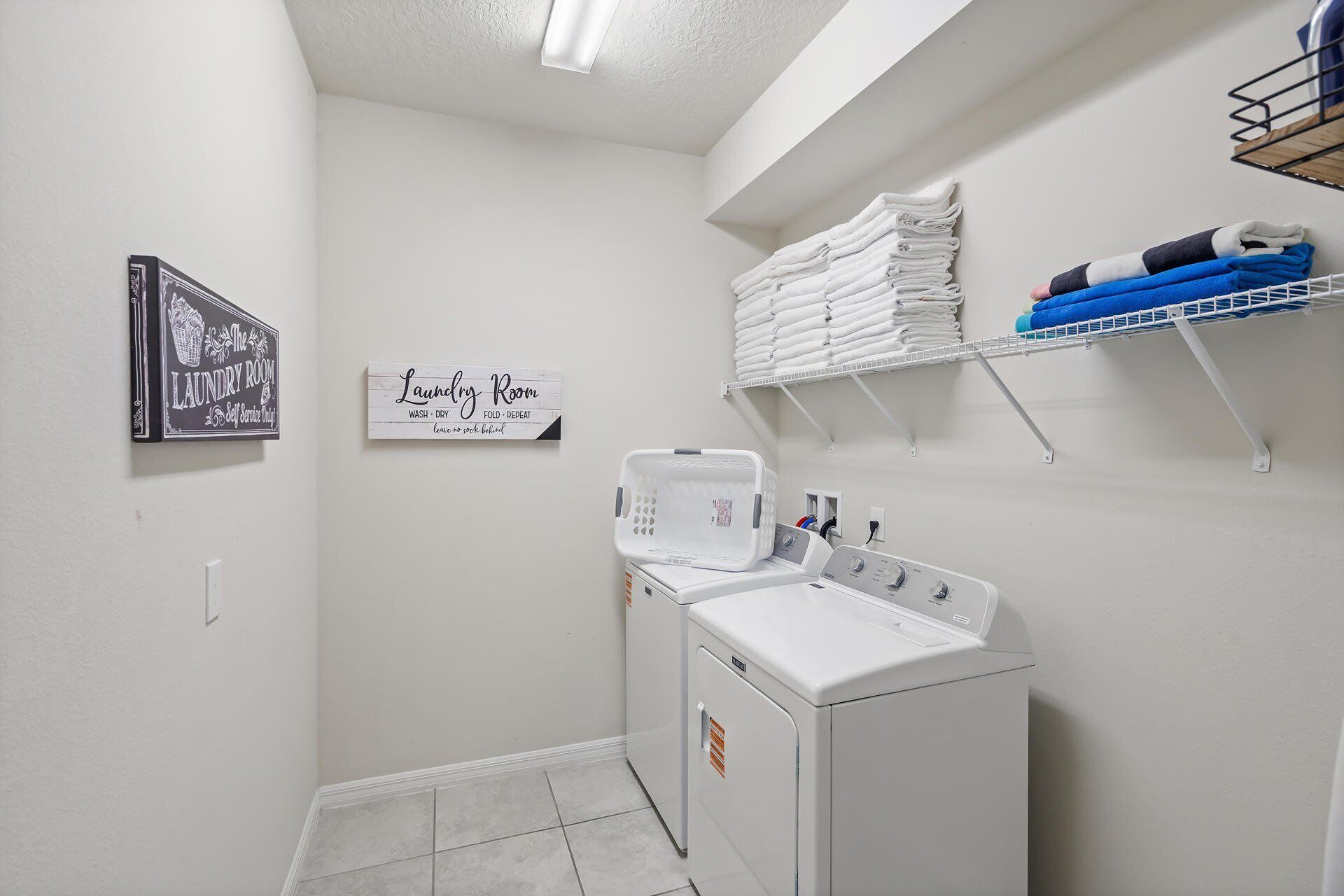 A laundry room with a washing machine, stacked towels, and a sign indicating self-service laundry.