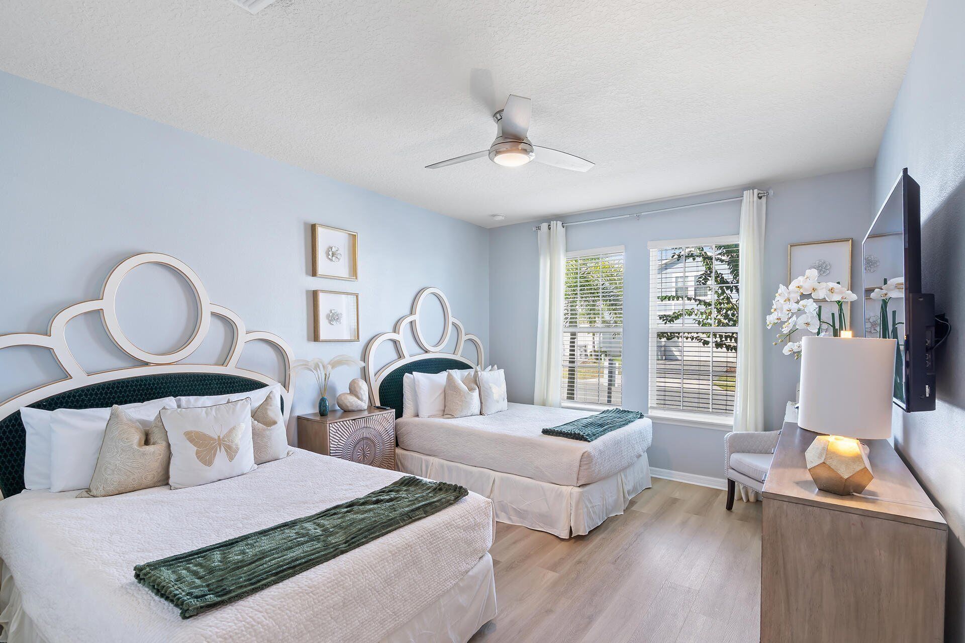 A bedroom with two beds, a ceiling fan, a TV, and a window with blinds.