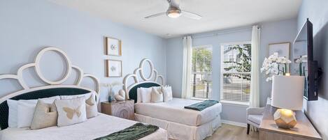 A bedroom with two beds, a ceiling fan, a TV, and a window with blinds.