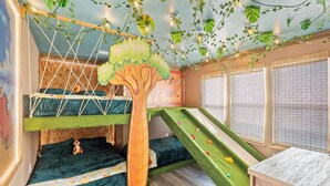 Uma sala de jogos infantil com área de recreação com tema de árvore, uma cama beliche e um escorrega.