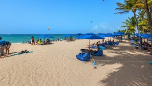 Ein Strand mit blauen Sonnenschirmen, Liegestühlen und entspannten Menschen.