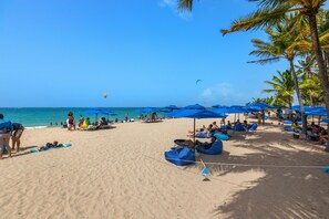 A beach with blue umbrellas, lounge chairs, and people relaxing. - Beachside Retreat with Pool - Sleeps 4 (San Juan)