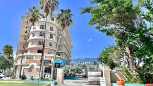 Ein mehrstöckiges Hotel mit geschwungener Fassade, Palmen und blauem Himmel.