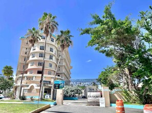 A multi-story hotel with a curved facade, palm trees, and a clear blue sky. - Beachside Retreat with Pool - Sleeps 4 (San Juan)