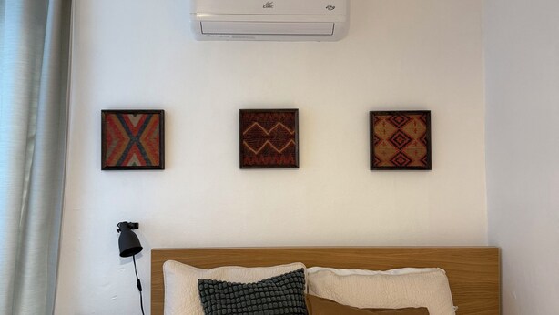 A hotel room with a bed, a wall-mounted air conditioner, and three decorative wall hangings. - Cozy Studio 2@Casa Marvella / Water Tank (San Juan)
