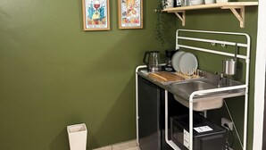 A compact kitchen with a sink, a microwave, and a small countertop. There are two framed artworks on the wall and a woven basket on a shelf. - Cozy Studio 2@Casa Marvella / Water Tank (San Juan)
